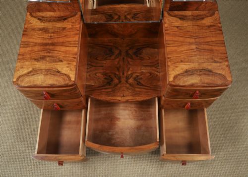 fig 10. An Art Deco figured walnut dressing table featuring twin pedestal drawers, a central curved drawer, red handles, and a three-panel upright mirror.