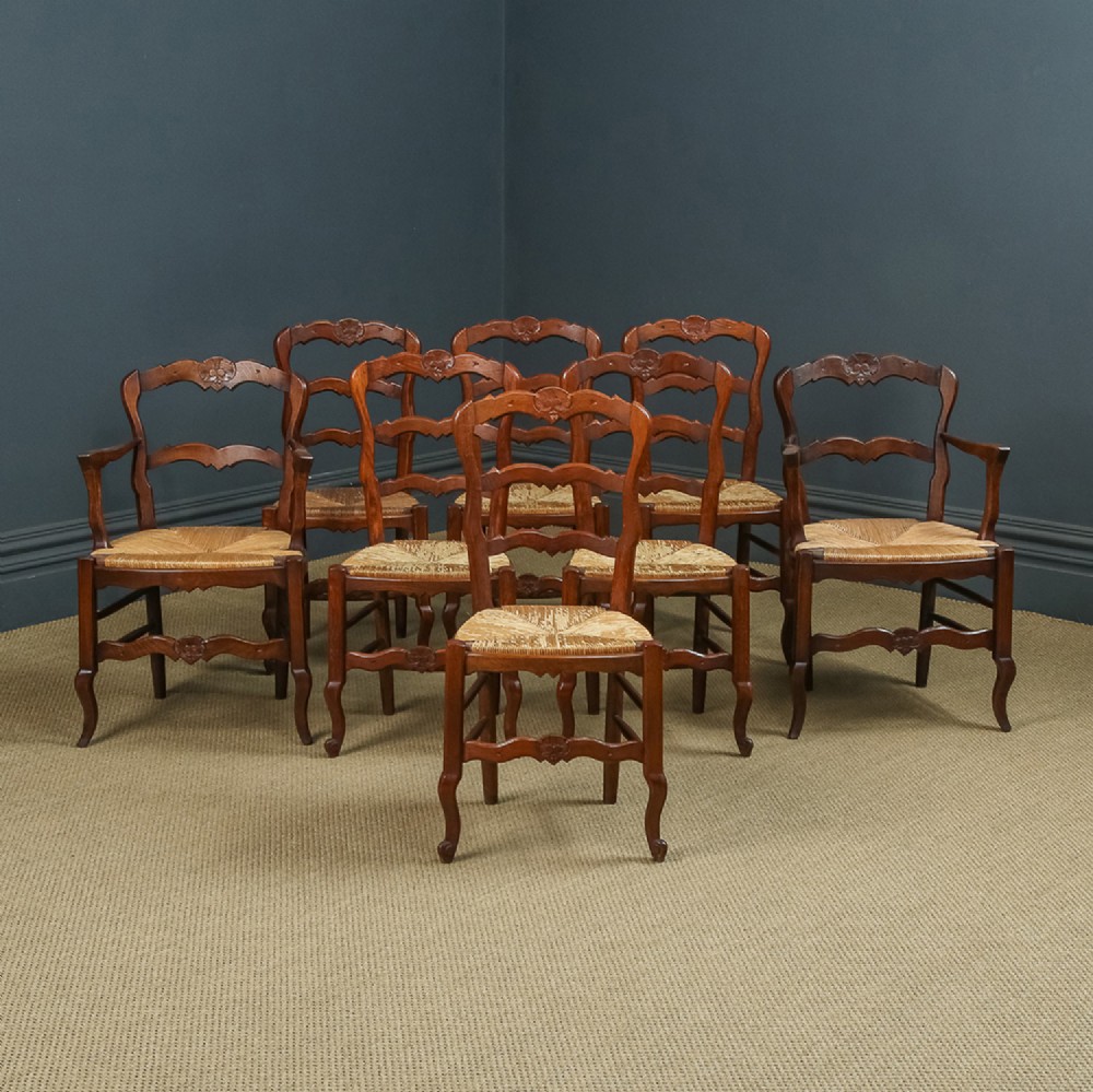 A set of eight French provincial oak dining chairs featuring wavy ladder backrests, hand-woven rush seats, and carved cabriole legs.