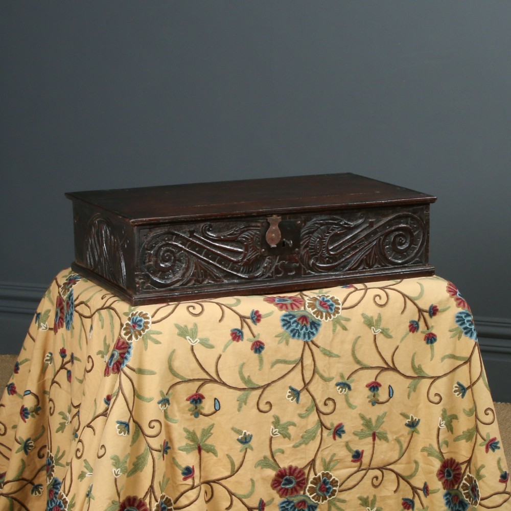 A dark brown 17th-century carved oak bible box featuring intricate scrollwork on the front panel and a central iron keyhole escutcheon.