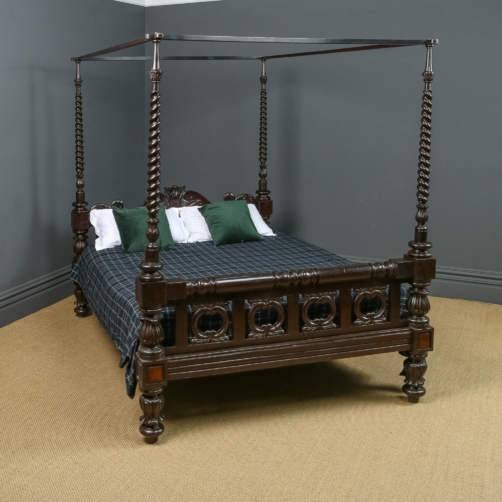 A dark brown Anglo-Indian colonial four poster bed with spiral turned posts and a carved wooden footboard.