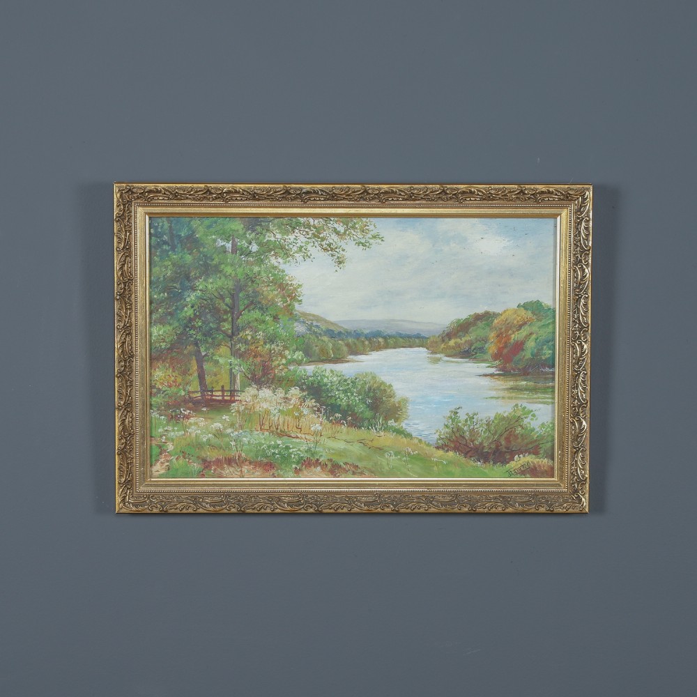 A framed landscape painting depicting a serene river flowing through green foliage and trees, presented in an ornate gilt frame.