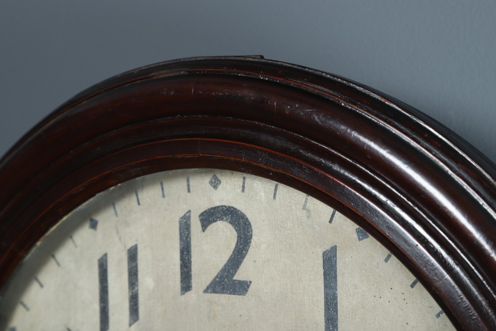 A large circular antique wall clock featuring a dark mahogany wooden surround, an off-white dial with bold black Arabic numerals, and twin winding keyholes. View IV