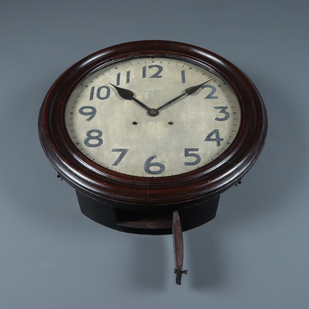 A large circular antique wall clock featuring a dark mahogany wooden surround, an off-white dial with bold black Arabic numerals, and twin winding keyholes. View VI