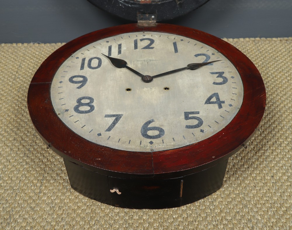 A large circular antique wall clock featuring a dark mahogany wooden surround, an off-white dial with bold black Arabic numerals, and twin winding keyholes. View VIII