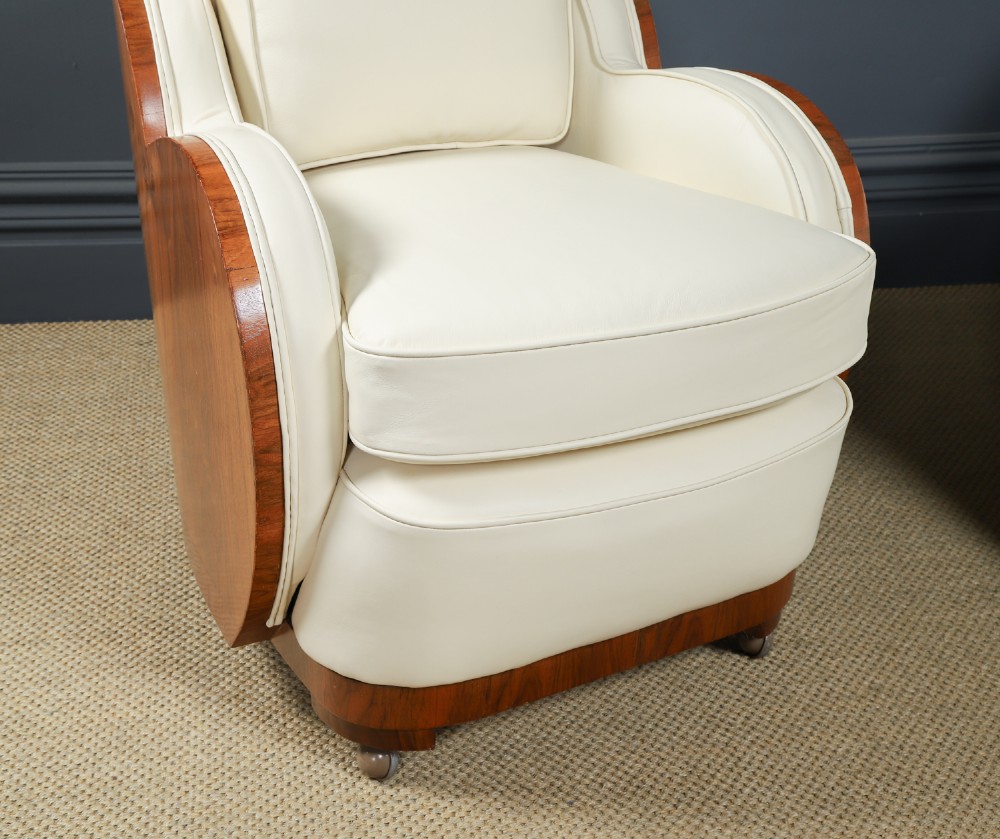 An antique Art Deco three-piece lounge suite consisting of a three-seater sofa and two matching armchairs upholstered in cream leather with curved walnut side panels. View IV