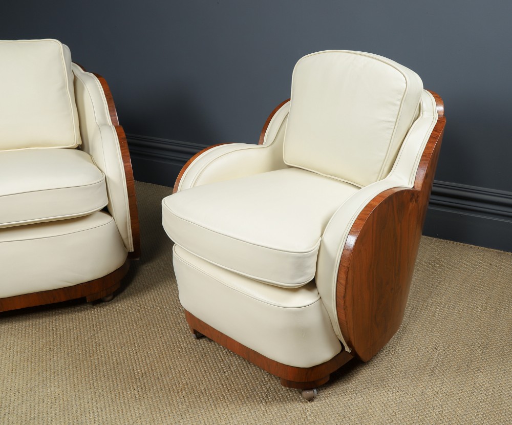 An antique Art Deco three-piece lounge suite consisting of a three-seater sofa and two matching armchairs upholstered in cream leather with curved walnut side panels. View X