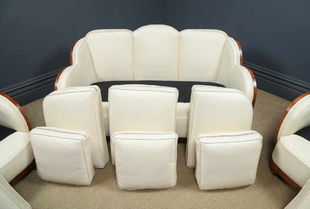 An antique Art Deco three-piece lounge suite consisting of a three-seater sofa and two matching armchairs upholstered in cream leather with curved walnut side panels. View XI