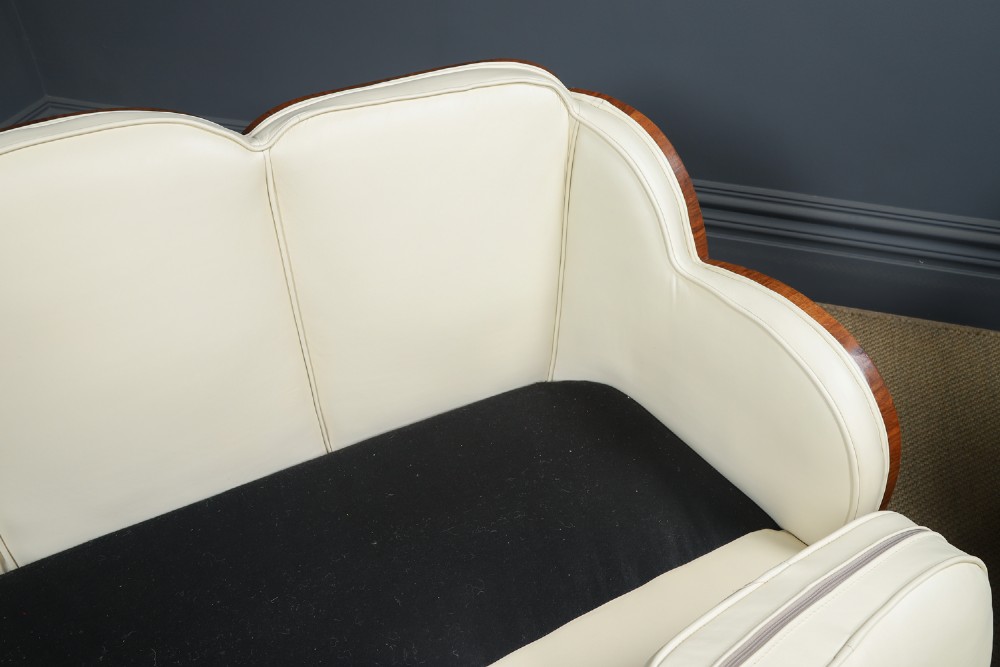 An antique Art Deco three-piece lounge suite consisting of a three-seater sofa and two matching armchairs upholstered in cream leather with curved walnut side panels. View XII