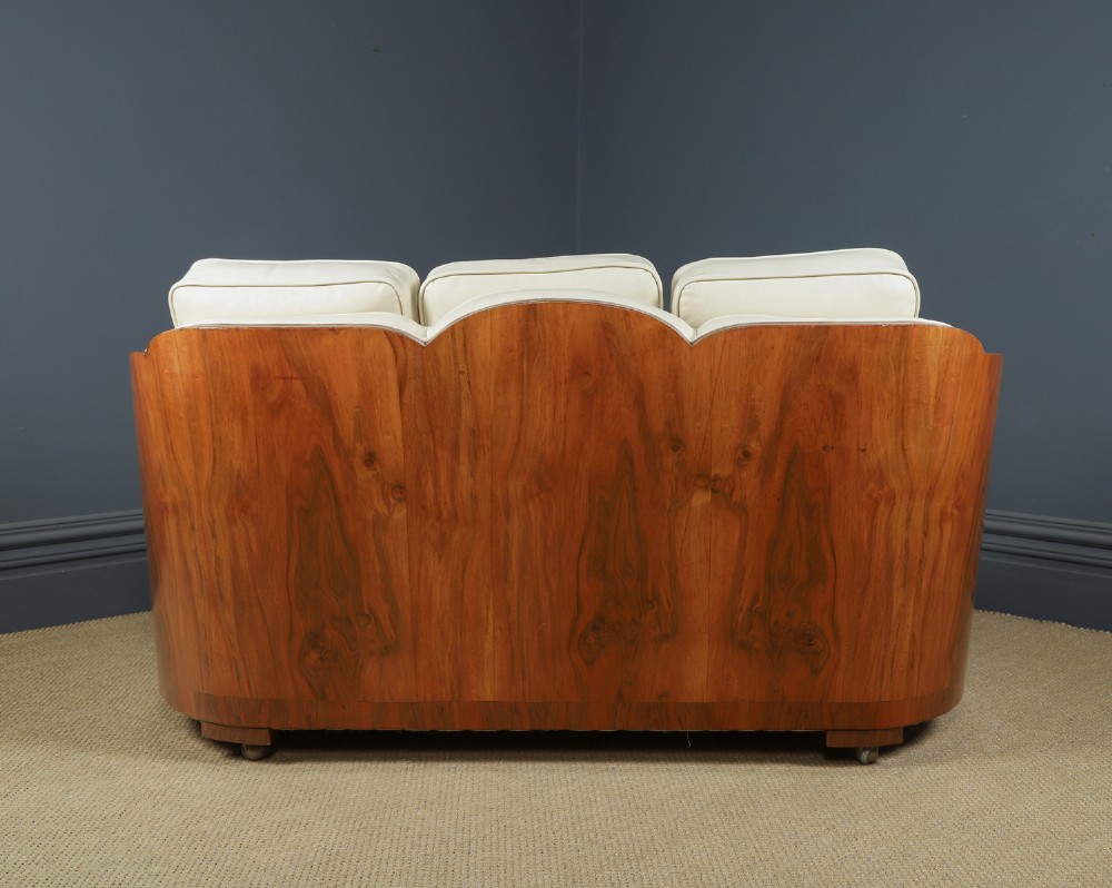 An antique Art Deco three-piece lounge suite consisting of a three-seater sofa and two matching armchairs upholstered in cream leather with curved walnut side panels. View XIII