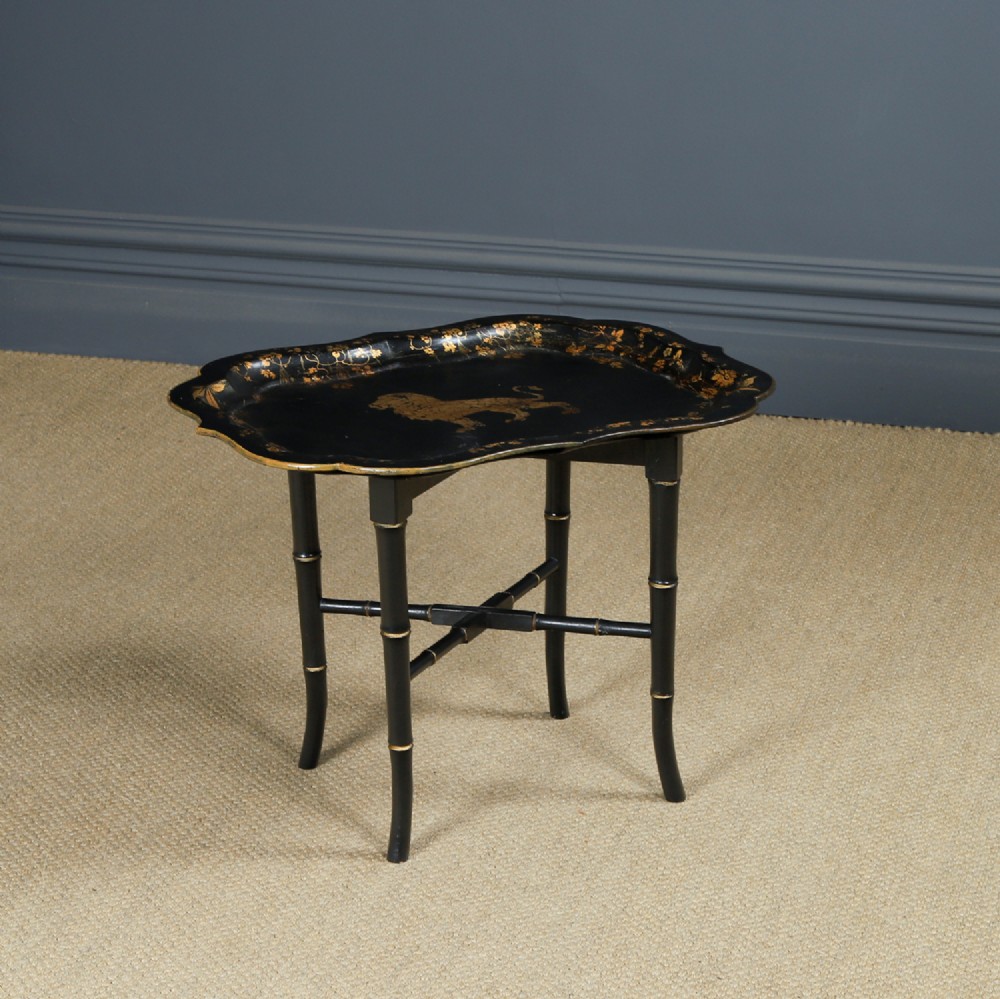 An ebonised Victorian papier-mache tray table featuring gilt Chinoiserie decoration and a lion motif, resting on a faux-bamboo base.