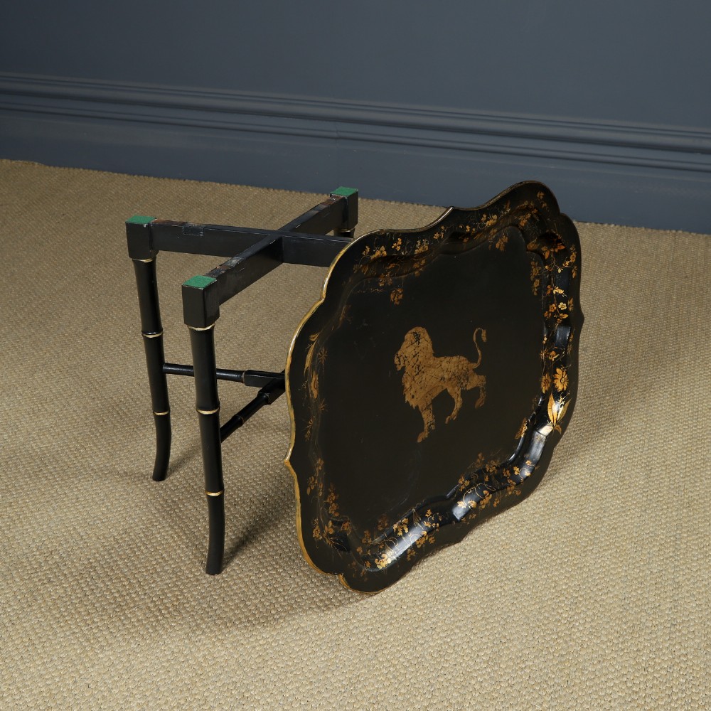 An ebonised Victorian papier-mache tray table featuring gilt Chinoiserie decoration and a lion motif, resting on a faux-bamboo base. View X