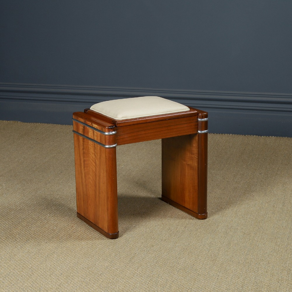 An Art Deco rectangular walnut stool featuring slab legs with metal band accents and a cream leather padded seat.