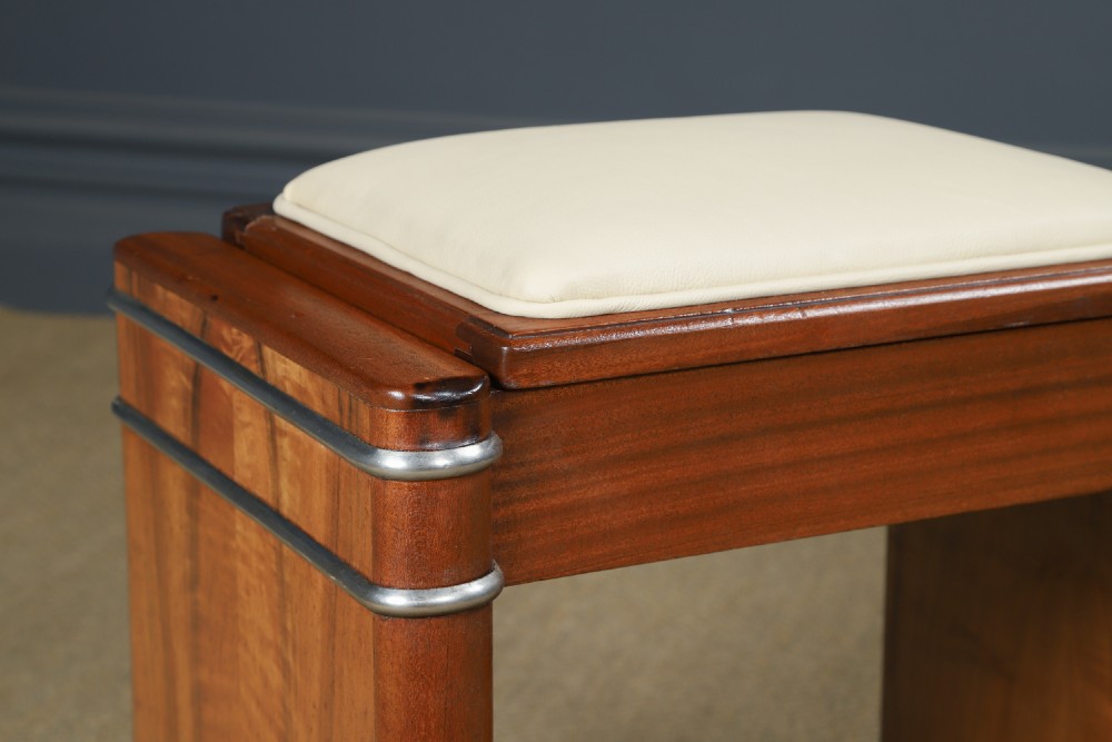 An Art Deco rectangular walnut stool featuring slab legs with metal band accents and a cream leather padded seat. View III