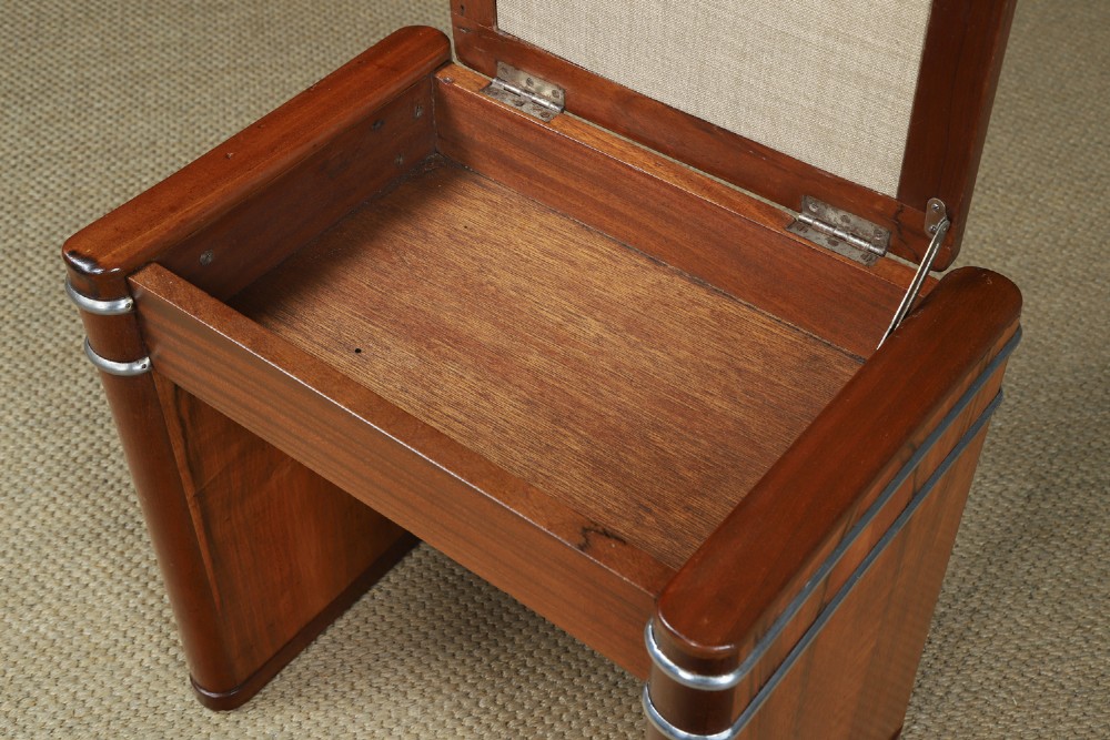 An Art Deco rectangular walnut stool featuring slab legs with metal band accents and a cream leather padded seat. View IX
