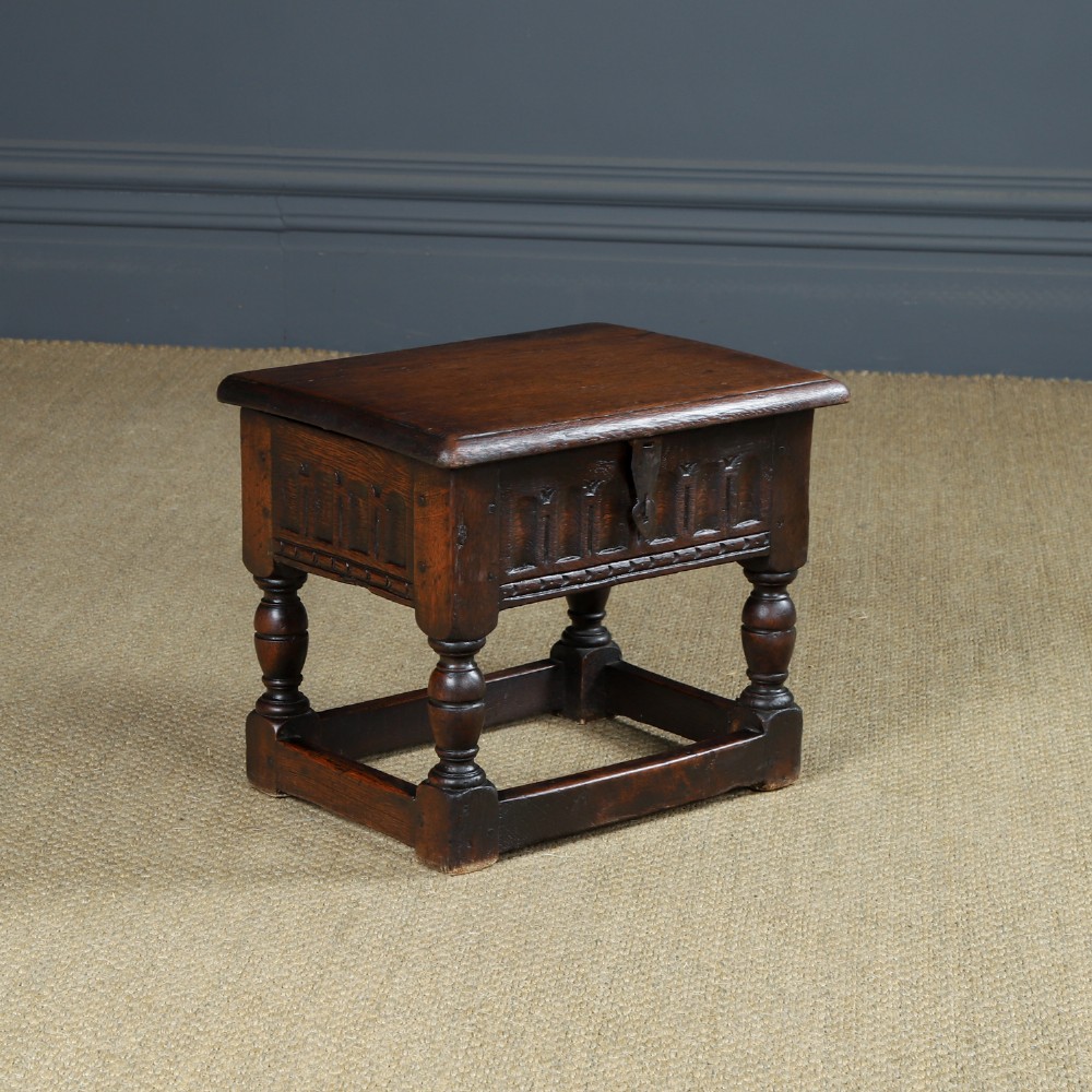 A small antique dark oak box stool featuring a hinged top lid, hand-carved frieze panels, turned legs, and square perimeter stretchers.
