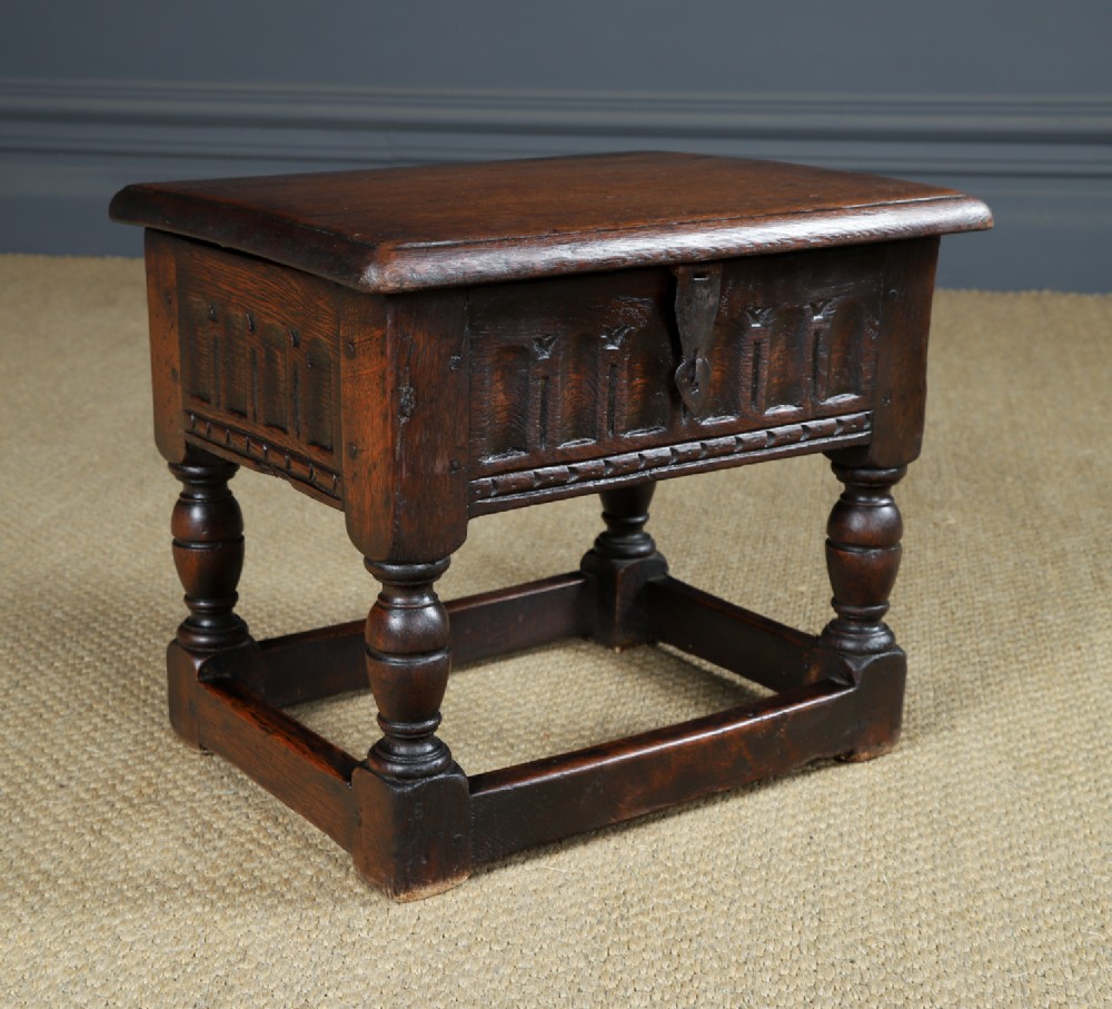 A small antique dark oak box stool featuring a hinged top lid, hand-carved frieze panels, turned legs, and square perimeter stretchers. View II