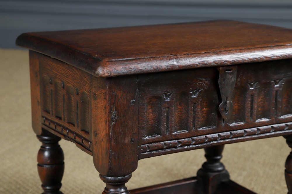 A small antique dark oak box stool featuring a hinged top lid, hand-carved frieze panels, turned legs, and square perimeter stretchers. View III