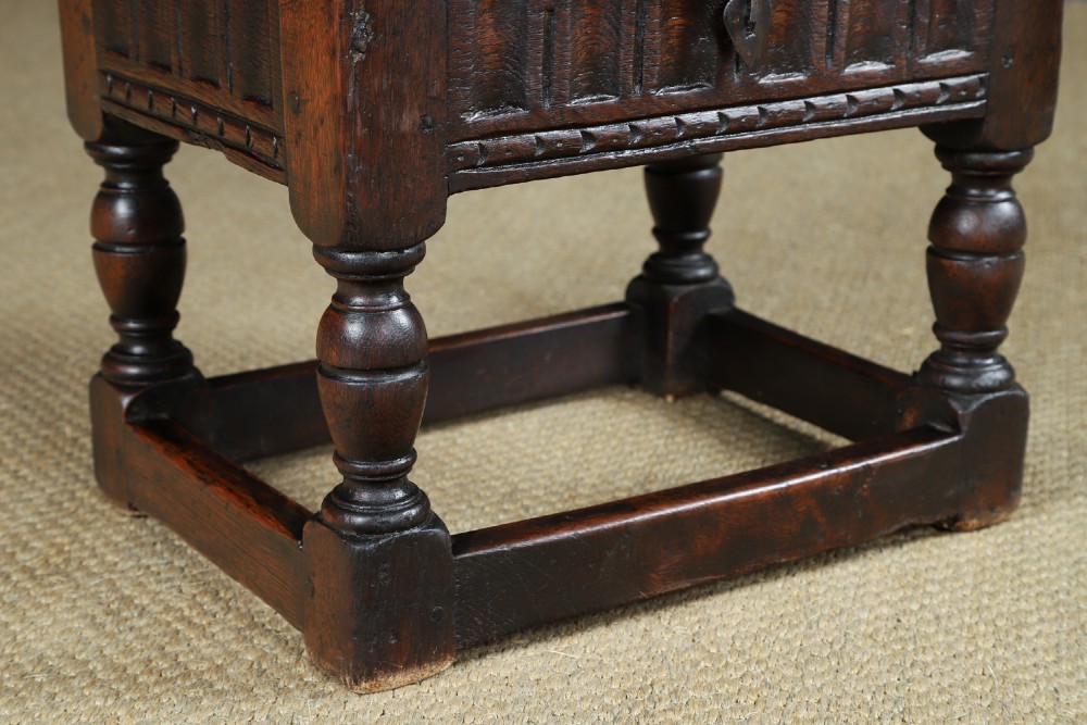 A small antique dark oak box stool featuring a hinged top lid, hand-carved frieze panels, turned legs, and square perimeter stretchers. View IV