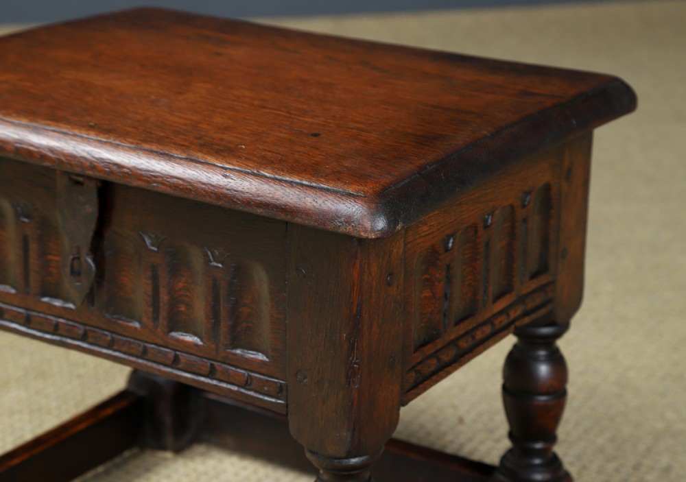 A small antique dark oak box stool featuring a hinged top lid, hand-carved frieze panels, turned legs, and square perimeter stretchers. View V