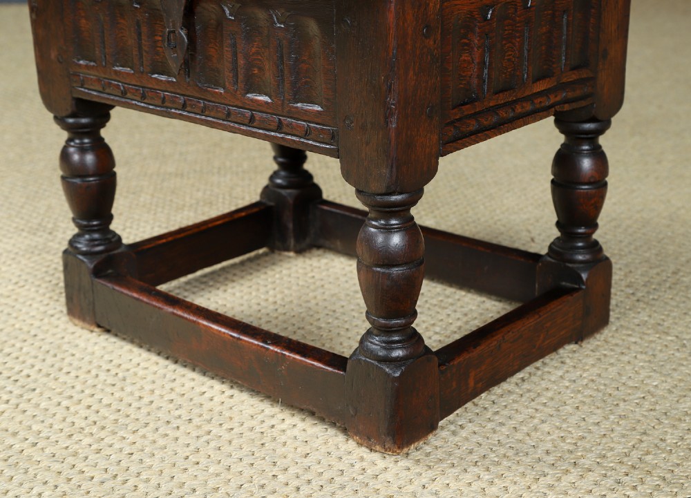 A small antique dark oak box stool featuring a hinged top lid, hand-carved frieze panels, turned legs, and square perimeter stretchers. View VI