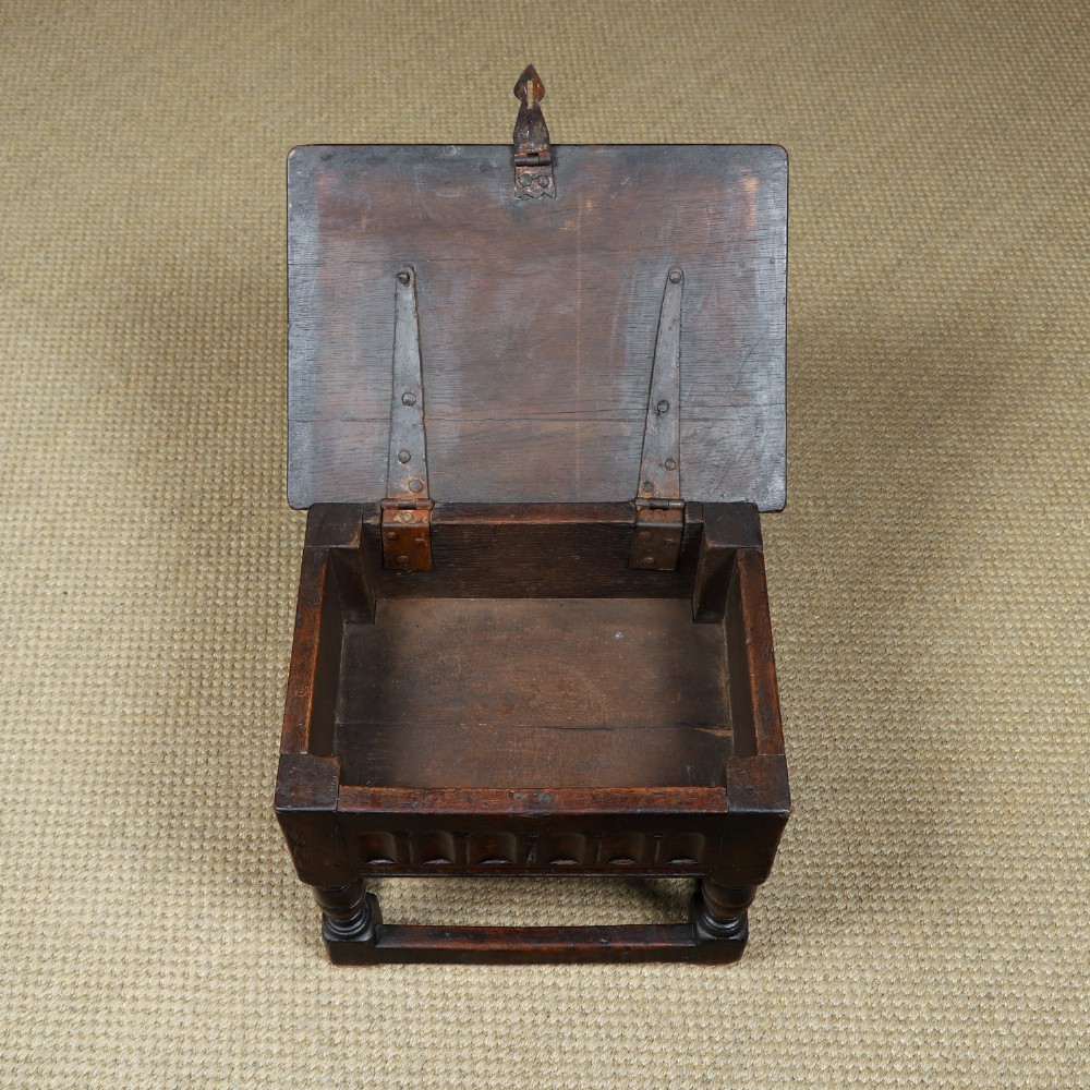 A small antique dark oak box stool featuring a hinged top lid, hand-carved frieze panels, turned legs, and square perimeter stretchers. View VII