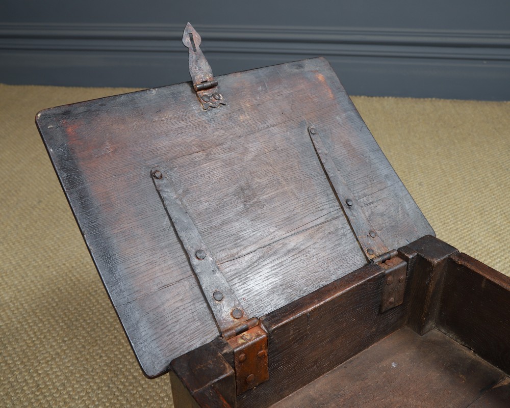 A small antique dark oak box stool featuring a hinged top lid, hand-carved frieze panels, turned legs, and square perimeter stretchers. View X