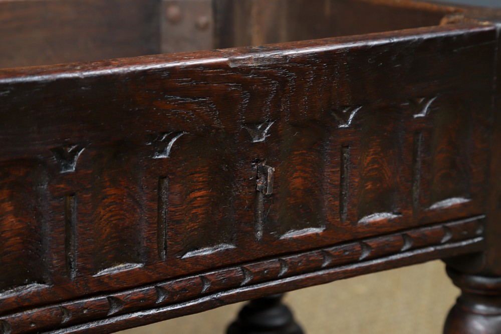 A small antique dark oak box stool featuring a hinged top lid, hand-carved frieze panels, turned legs, and square perimeter stretchers. View XI