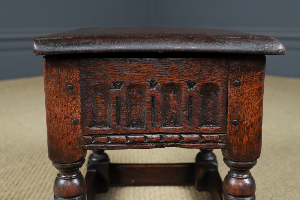 A small antique dark oak box stool featuring a hinged top lid, hand-carved frieze panels, turned legs, and square perimeter stretchers. View XIII