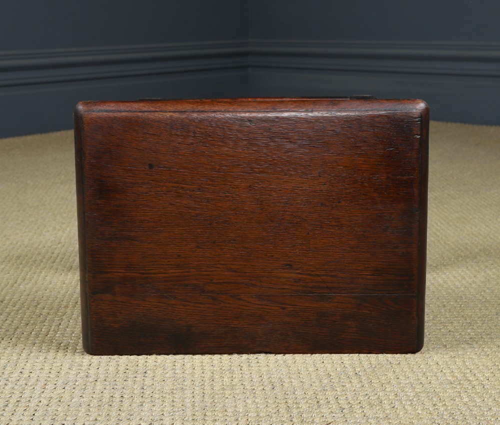 A small antique dark oak box stool featuring a hinged top lid, hand-carved frieze panels, turned legs, and square perimeter stretchers. View XV