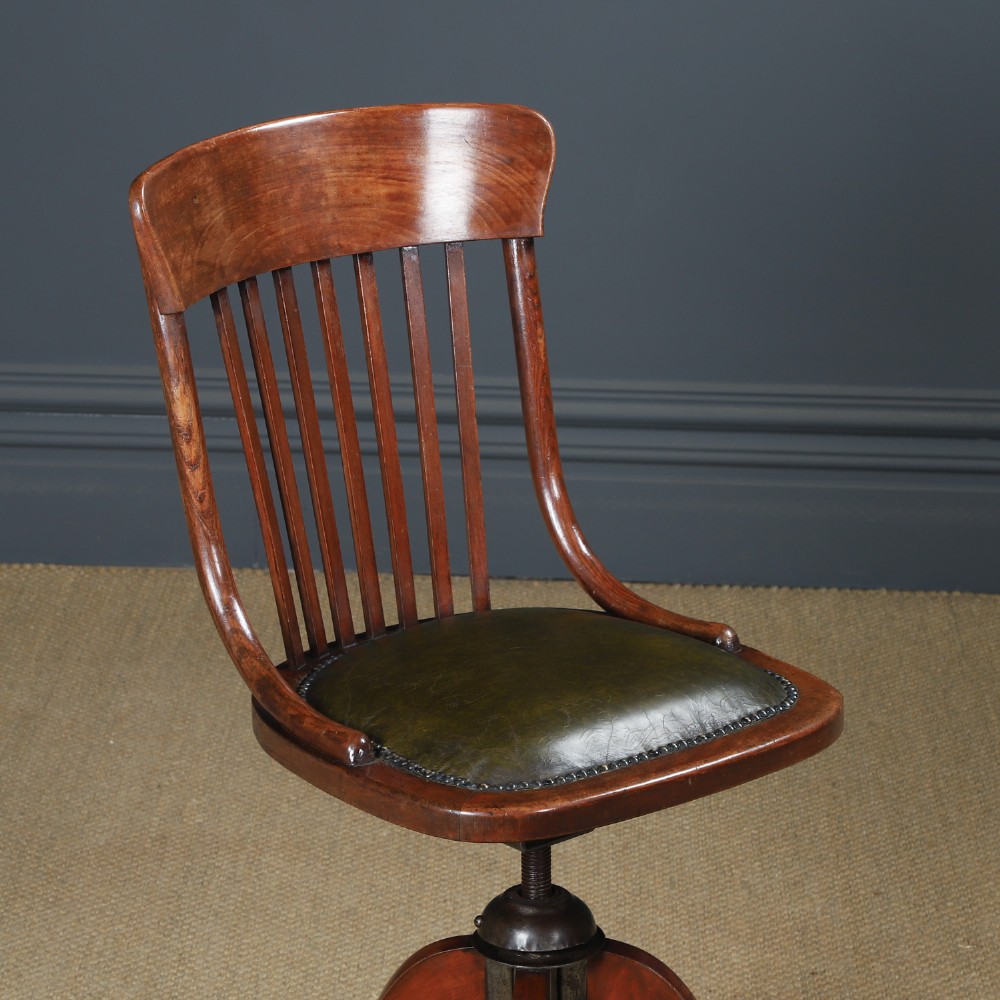 An antique George V stained beech revolving office chair featuring a slatted backrest, green leather seat, and splayed legs on brass castors. View II