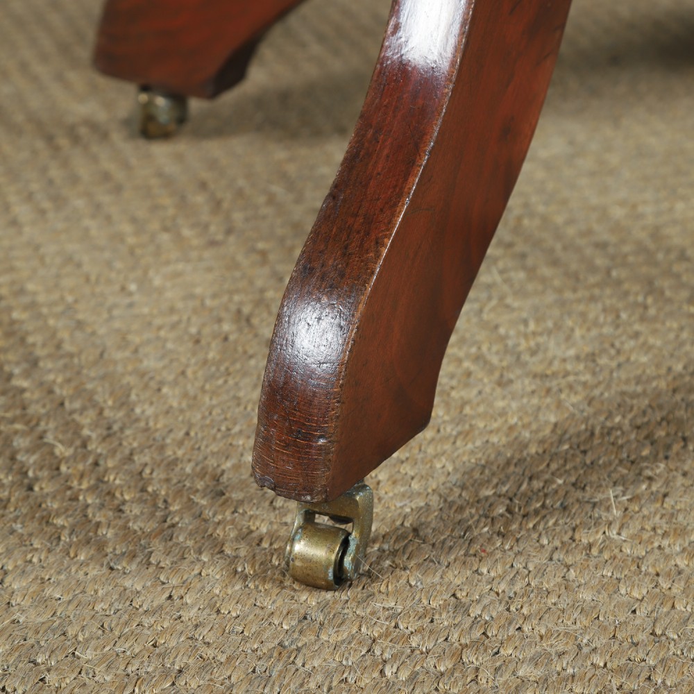 An antique George V stained beech revolving office chair featuring a slatted backrest, green leather seat, and splayed legs on brass castors. View III