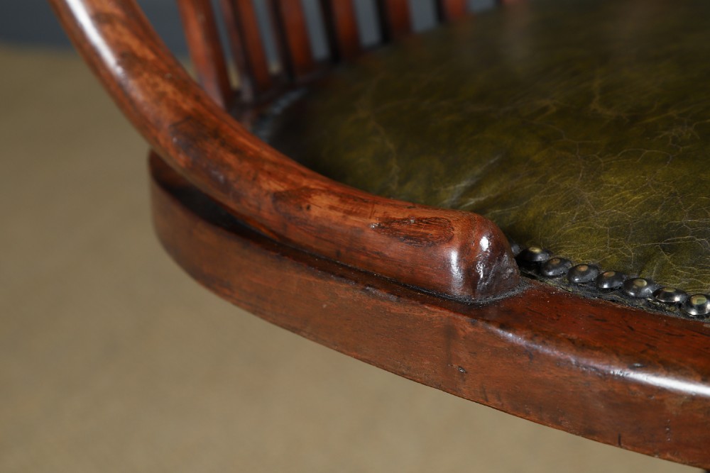 An antique George V stained beech revolving office chair featuring a slatted backrest, green leather seat, and splayed legs on brass castors. View VI