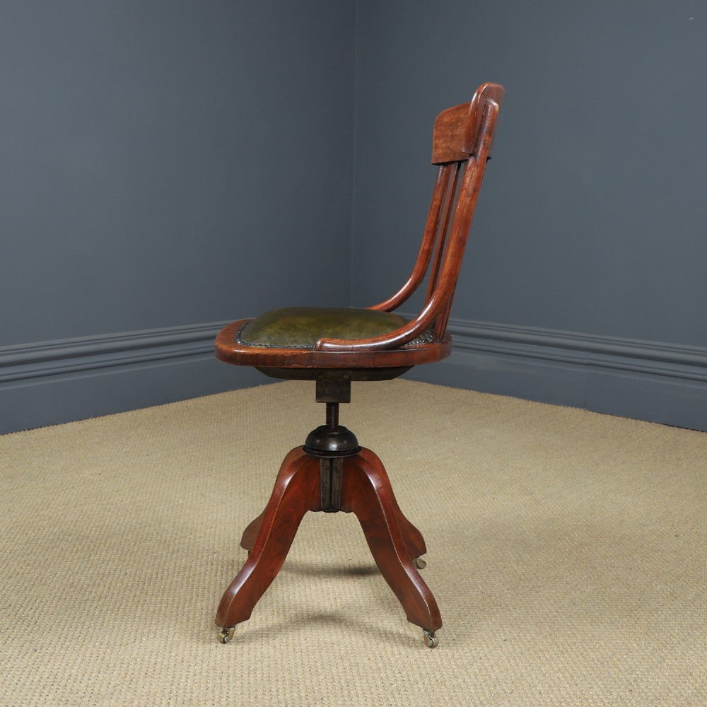 An antique George V stained beech revolving office chair featuring a slatted backrest, green leather seat, and splayed legs on brass castors. View VII