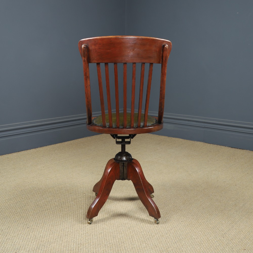 An antique George V stained beech revolving office chair featuring a slatted backrest, green leather seat, and splayed legs on brass castors. View VIII