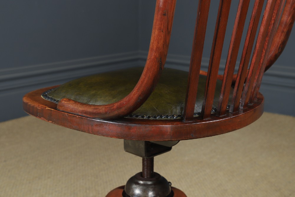 An antique George V stained beech revolving office chair featuring a slatted backrest, green leather seat, and splayed legs on brass castors. View X