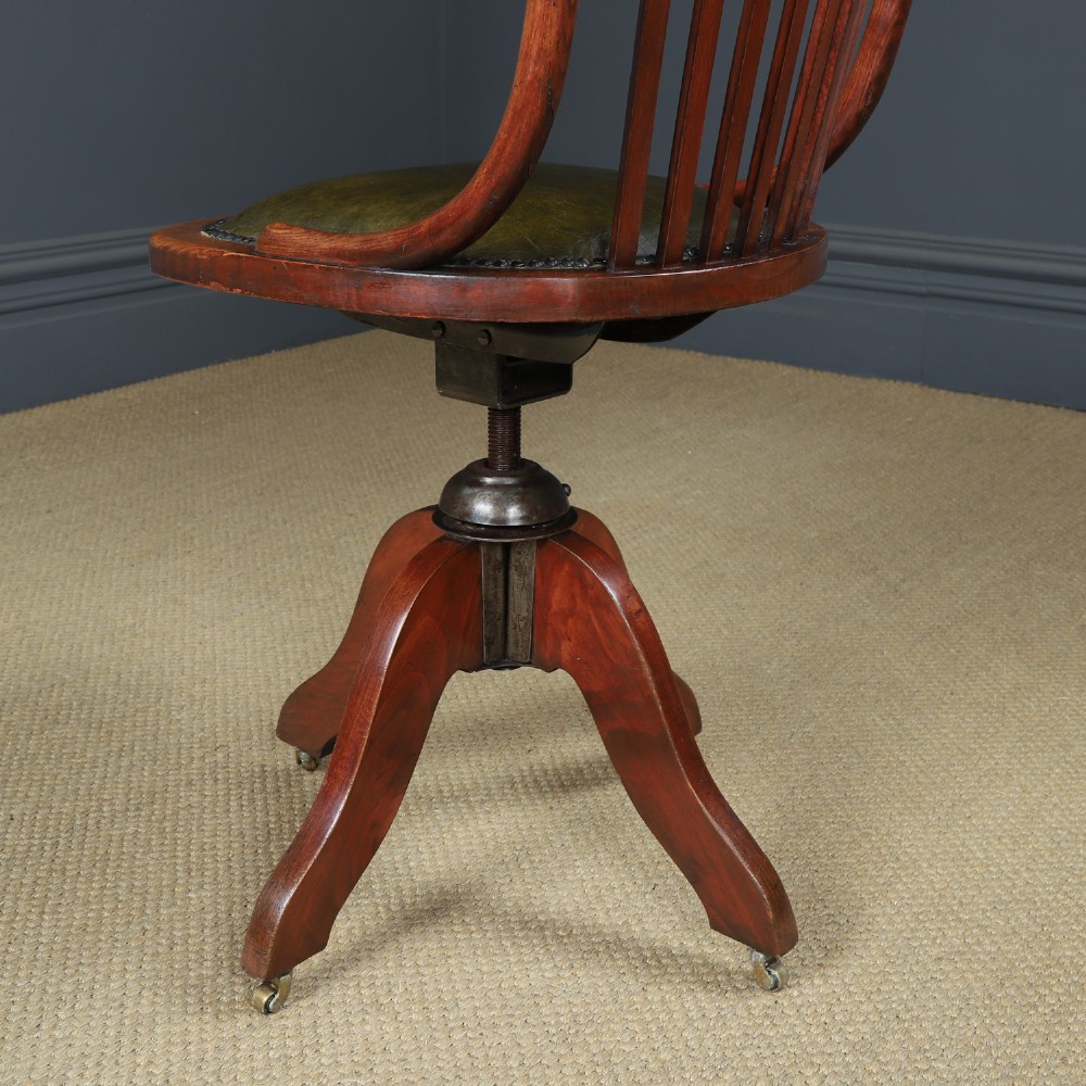 An antique George V stained beech revolving office chair featuring a slatted backrest, green leather seat, and splayed legs on brass castors. View XI