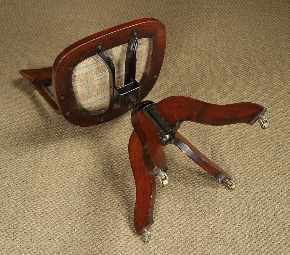 An antique George V stained beech revolving office chair featuring a slatted backrest, green leather seat, and splayed legs on brass castors. View XIII