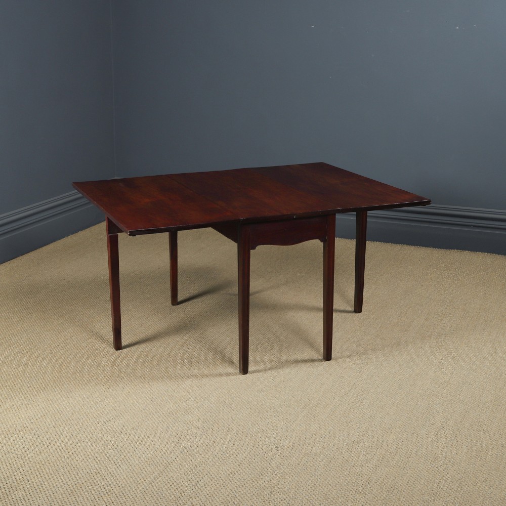 A Georgian mahogany drop-leaf dining table shown fully extended with rectangular flaps, a shaped apron, and straight square legs.