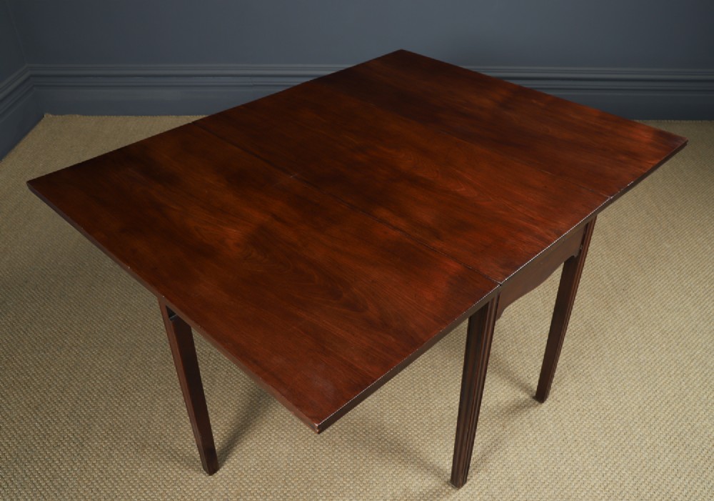 A Georgian mahogany drop-leaf dining table shown fully extended with rectangular flaps, a shaped apron, and straight square legs. View III