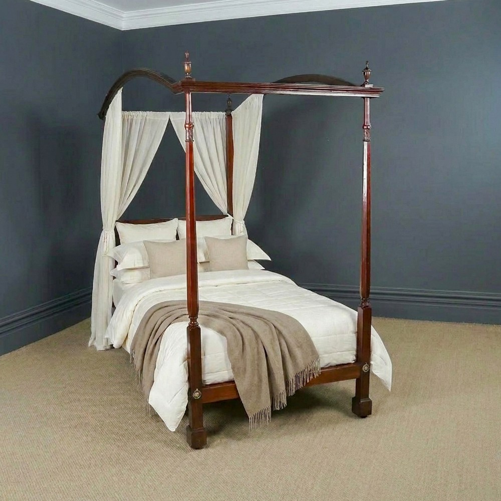 An Edwardian mahogany single four poster bed with turned posts, an arched canopy structure, and neutral drapery.