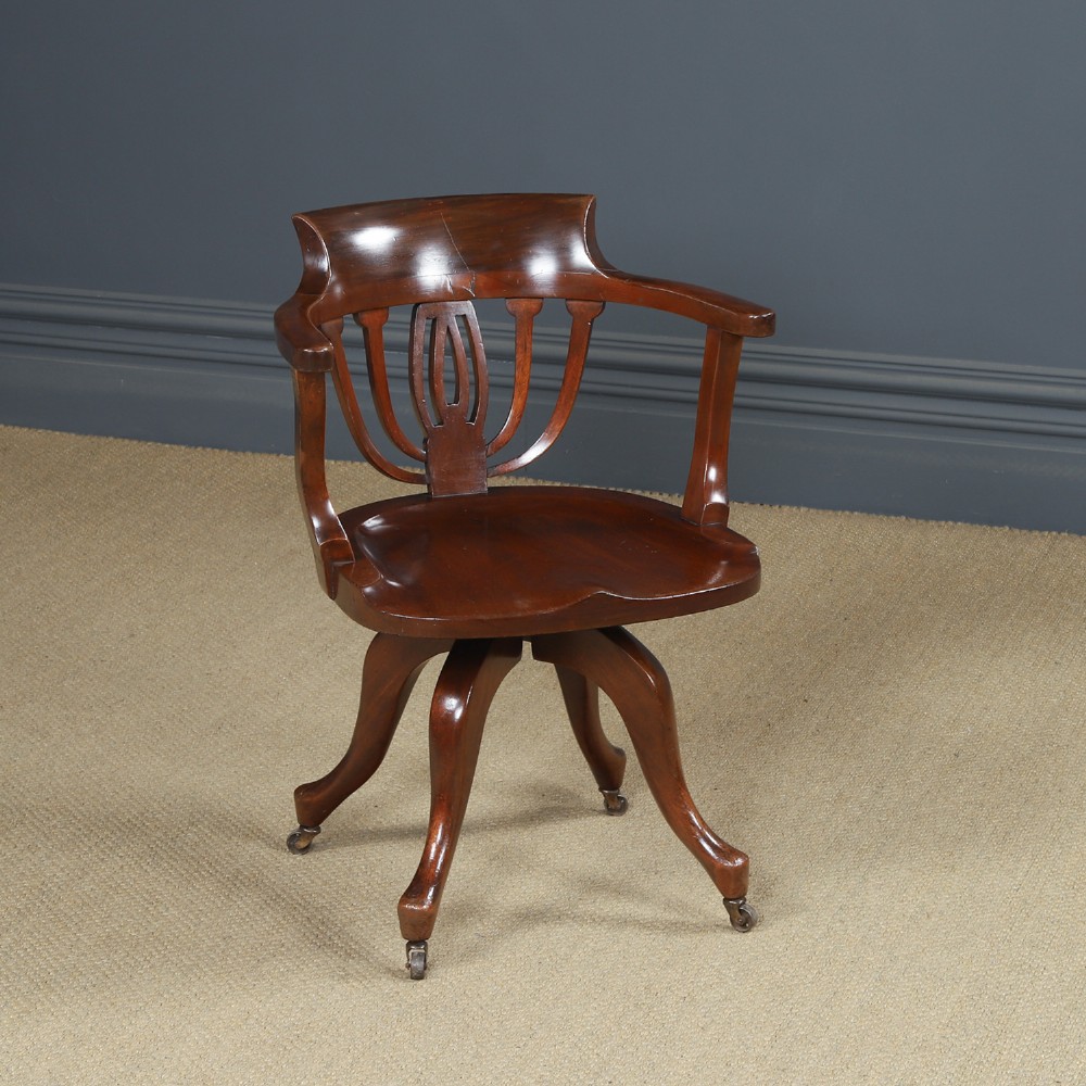 Victorian mahogany revolving desk armchair featuring a curved crest rail, pierced splat back, contoured wooden seat, and four legs with castors.