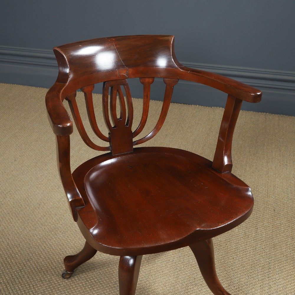 Victorian mahogany revolving desk armchair featuring a curved crest rail, pierced splat back, contoured wooden seat, and four legs with castors. View II