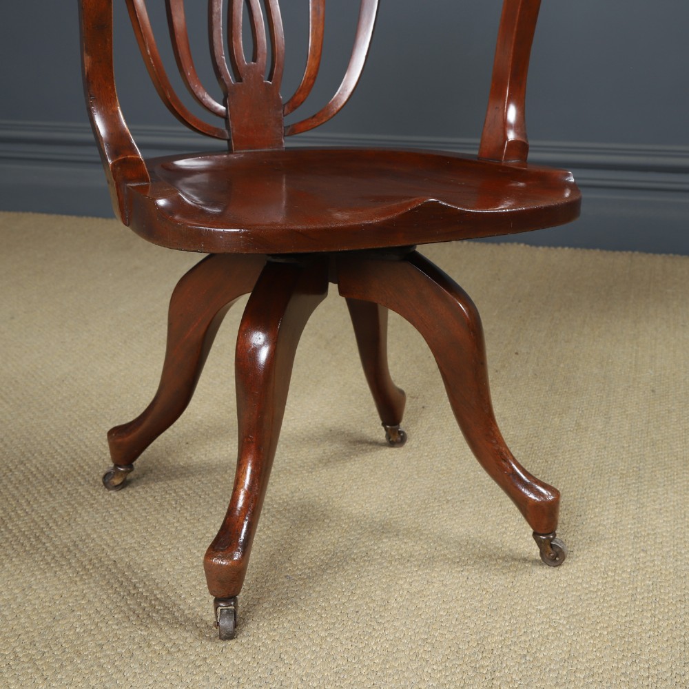 Victorian mahogany revolving desk armchair featuring a curved crest rail, pierced splat back, contoured wooden seat, and four legs with castors. View III