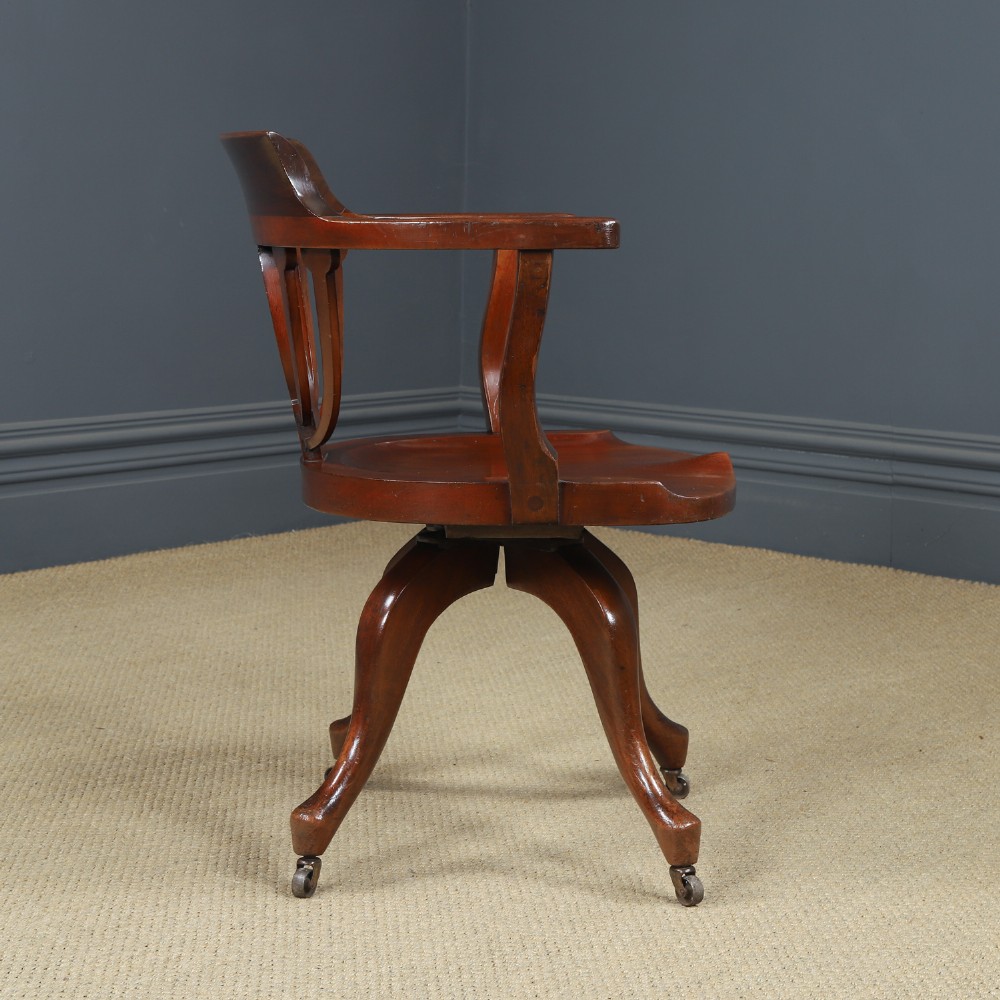 Victorian mahogany revolving desk armchair featuring a curved crest rail, pierced splat back, contoured wooden seat, and four legs with castors. View V