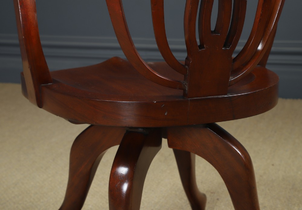 Victorian mahogany revolving desk armchair featuring a curved crest rail, pierced splat back, contoured wooden seat, and four legs with castors. View X