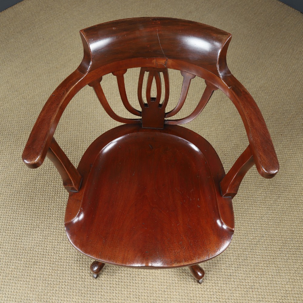 Victorian mahogany revolving desk armchair featuring a curved crest rail, pierced splat back, contoured wooden seat, and four legs with castors. View XI