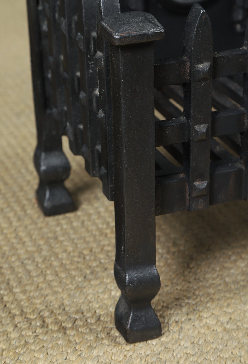 A black cast iron open fire grate featuring an arched backplate decorated with an urn relief and a palisade front basket resting on four square legs. View VI
