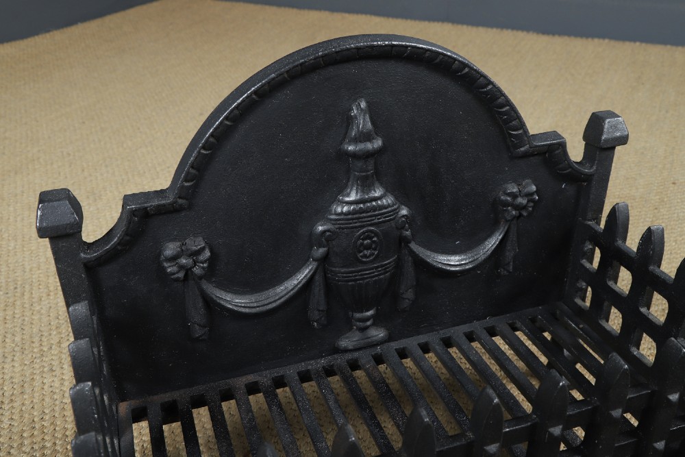A black cast iron open fire grate featuring an arched backplate decorated with an urn relief and a palisade front basket resting on four square legs. View VIII