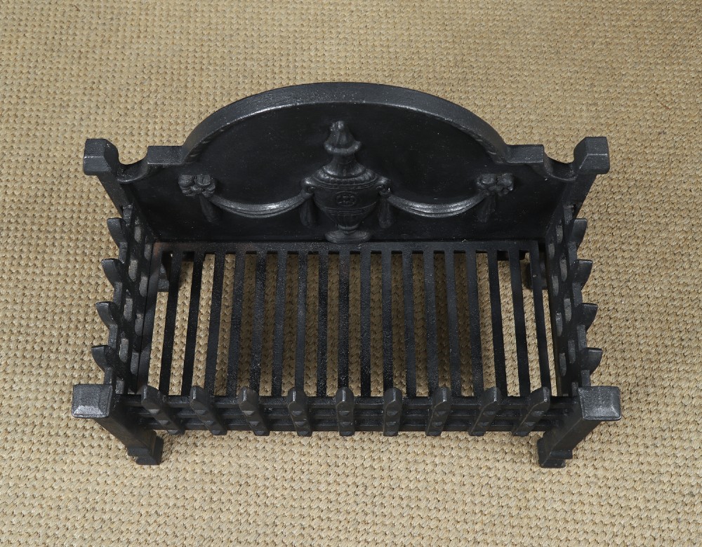 A black cast iron open fire grate featuring an arched backplate decorated with an urn relief and a palisade front basket resting on four square legs. View X