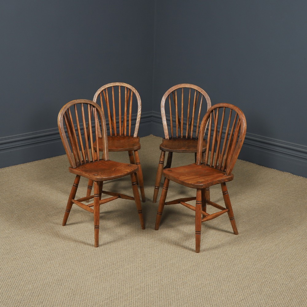 A set of four antique English warm brown ash and elm Windsor dining chairs featuring hoop backs, stick spindles, and turned legs.
